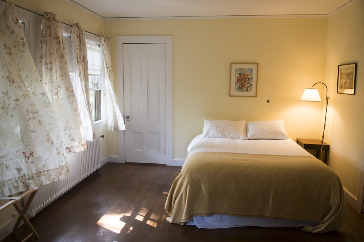 A bedroom with twin beds, period furniture and windows facing the water