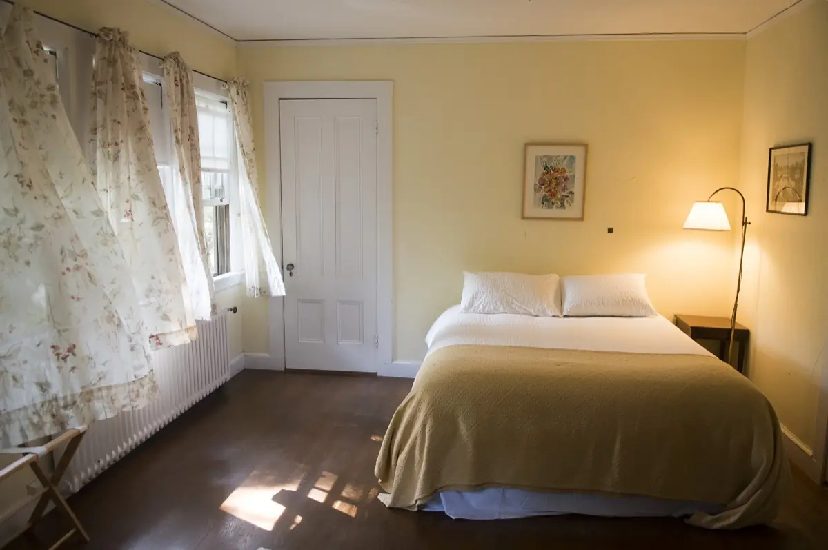 A bedroom with twin beds, period furniture and windows facing the water
