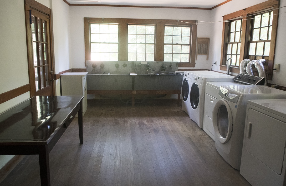 The laundry room, with washing machines and dryers along one wall, deep zinc utility sinks under the windows and a folding table