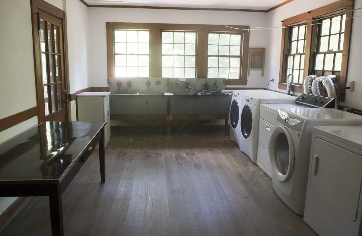 The laundry room, with washing machines and dryers along one wall, deep zinc utility sinks under the windows and a folding table