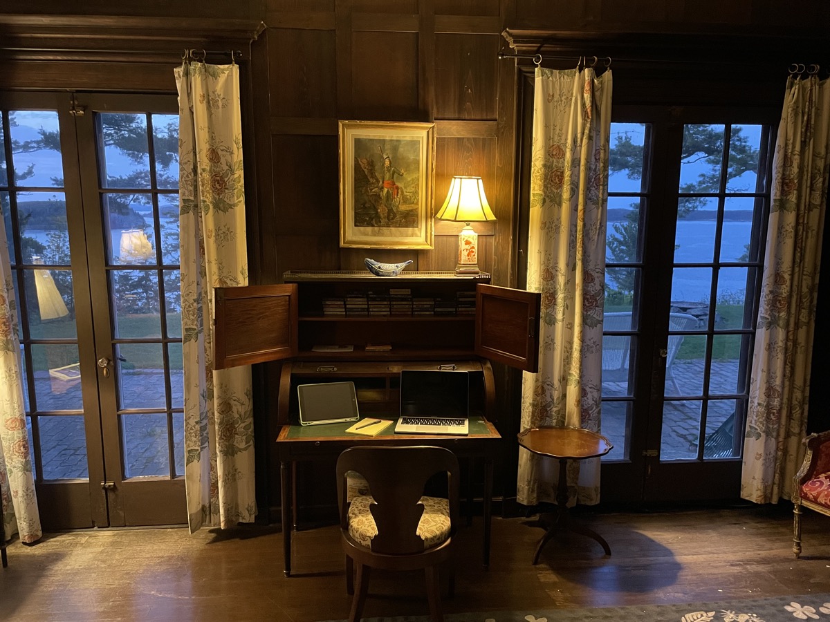A writing desk with a laptop and notepad, set between French doors looking out over Frenchman Bay at dusk