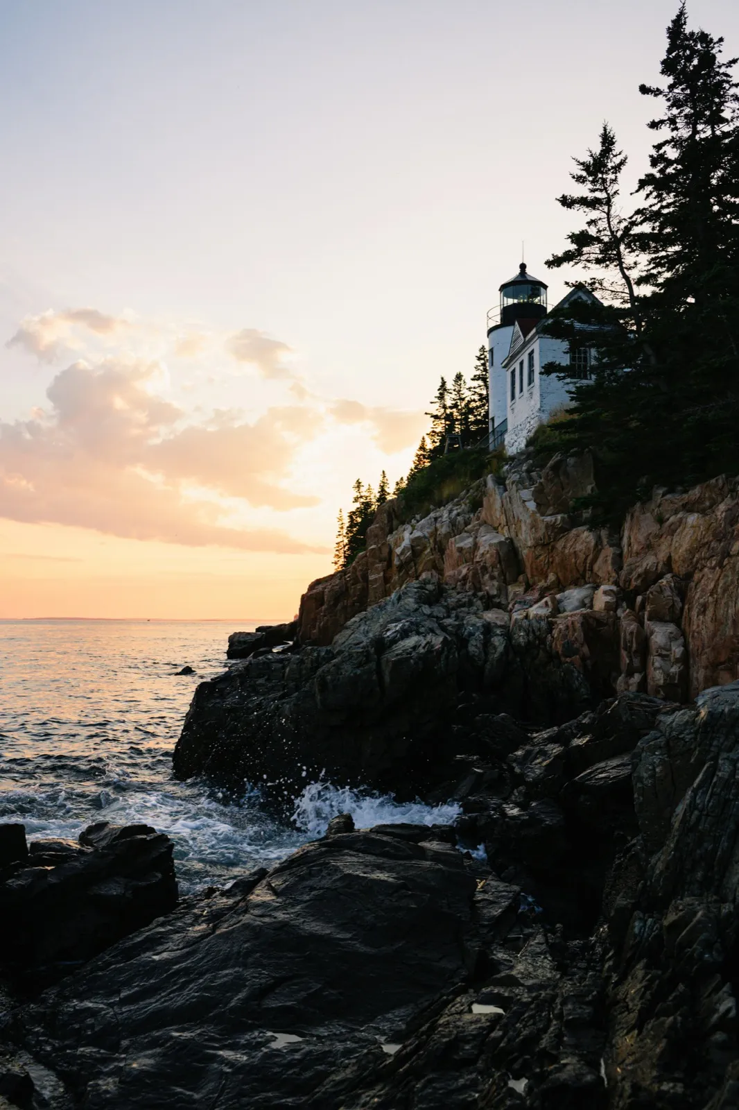 A lighthouse on the rocky Acadia shore at sunset