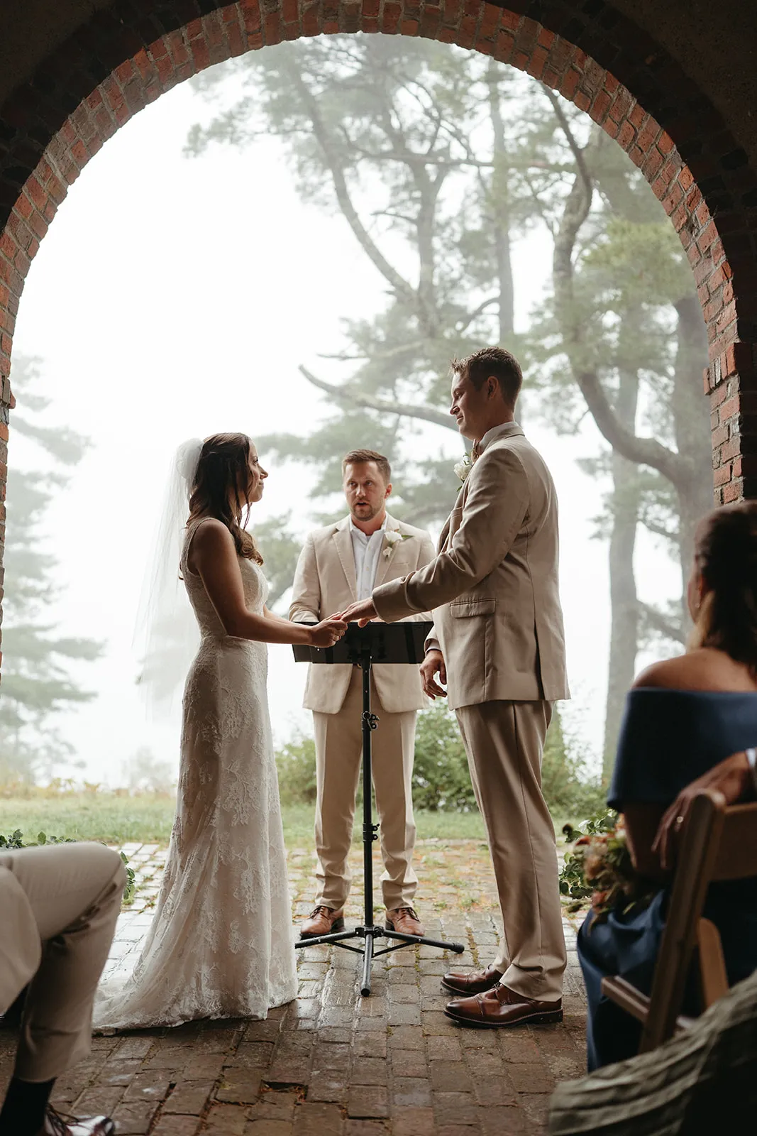 A couple exchanging vows under the brick arch at the end of the terrace, fog over Frenchman Bay behind them